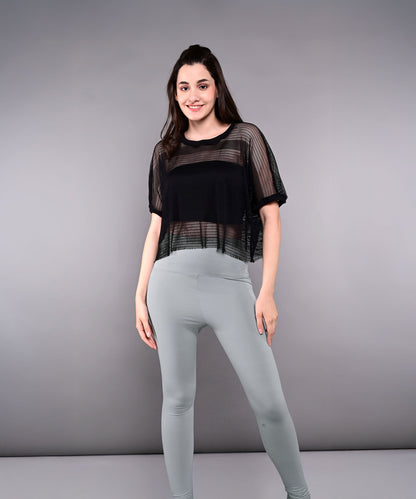 Woman smiles against a plain gray background wearing the Tuna Active Black Netted Top and light gray leggings.