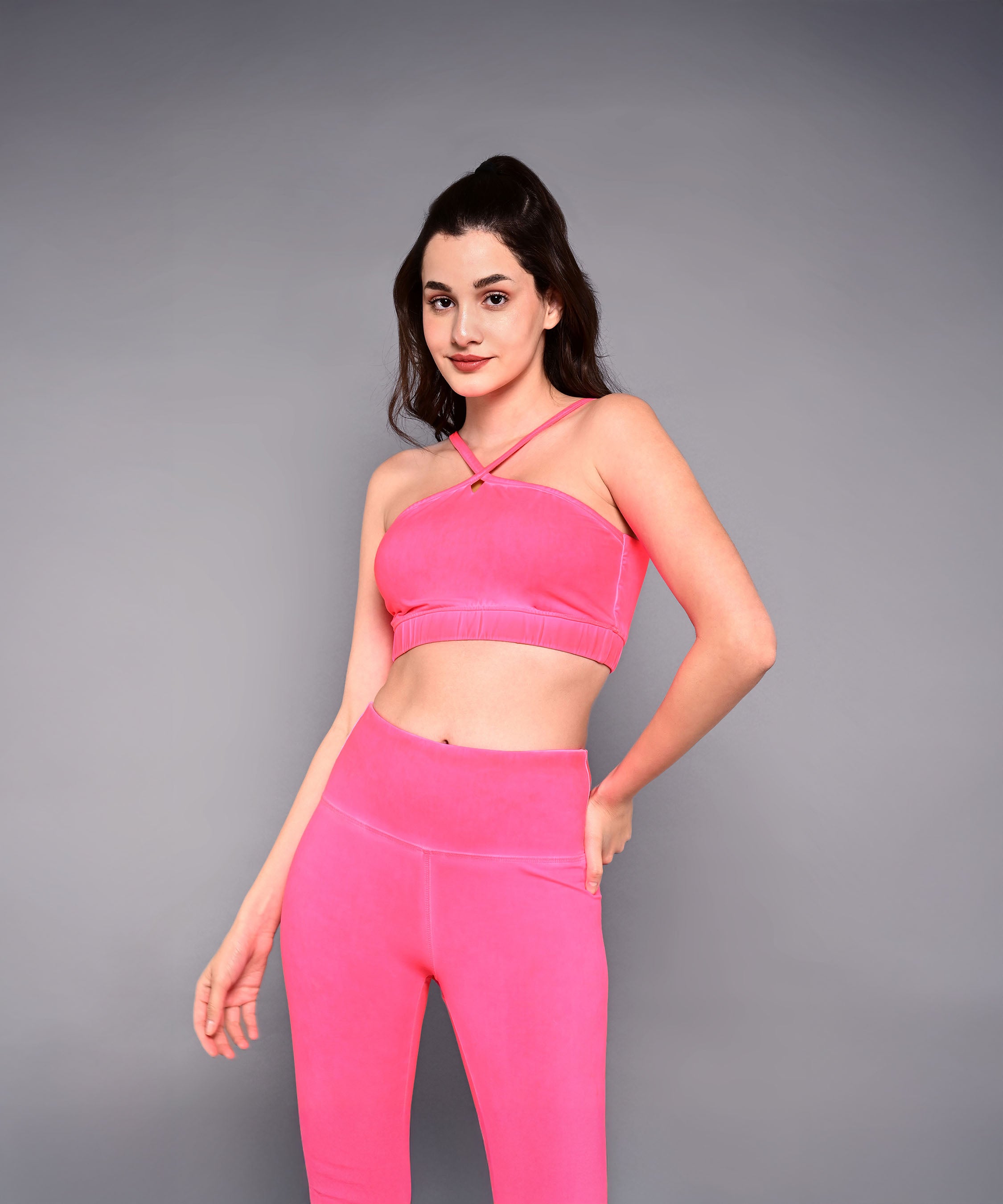 A woman poses against a plain grey background wearing the Neon Pink Sports Bra, made from skin-friendly cotton lycra, showcasing its vibrant colour.
