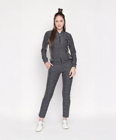 A woman stands against a white background, smiling and showcasing stylish Self Printed Grey TrackPants, featuring a dark gray athleisure look with patterned sides.