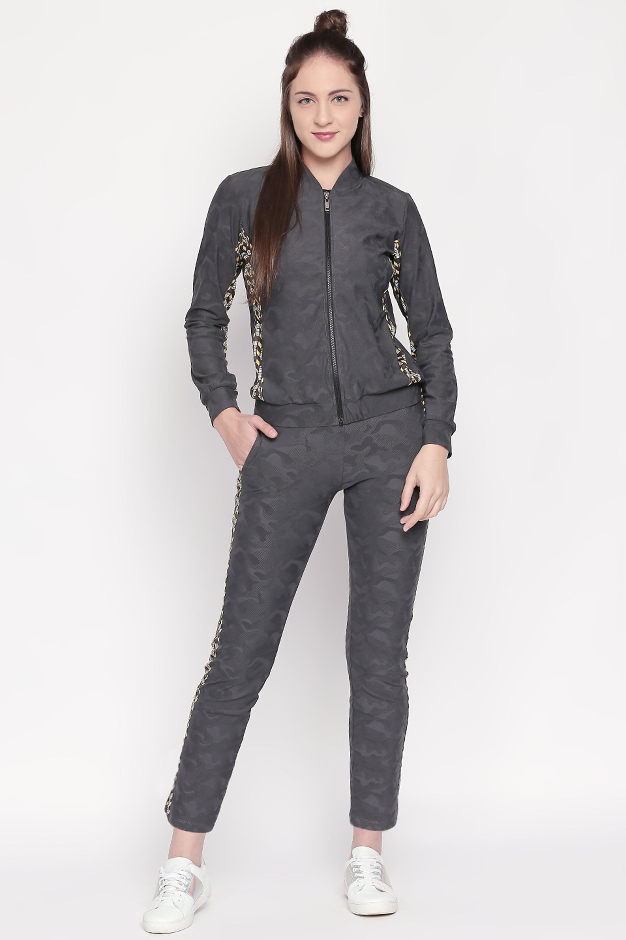 Woman in an Active Wear Printed Jacket in Grey from Tuna London, paired with matching dark grey tracksuit bottoms and white sneakers, standing with one hand in her pocket.