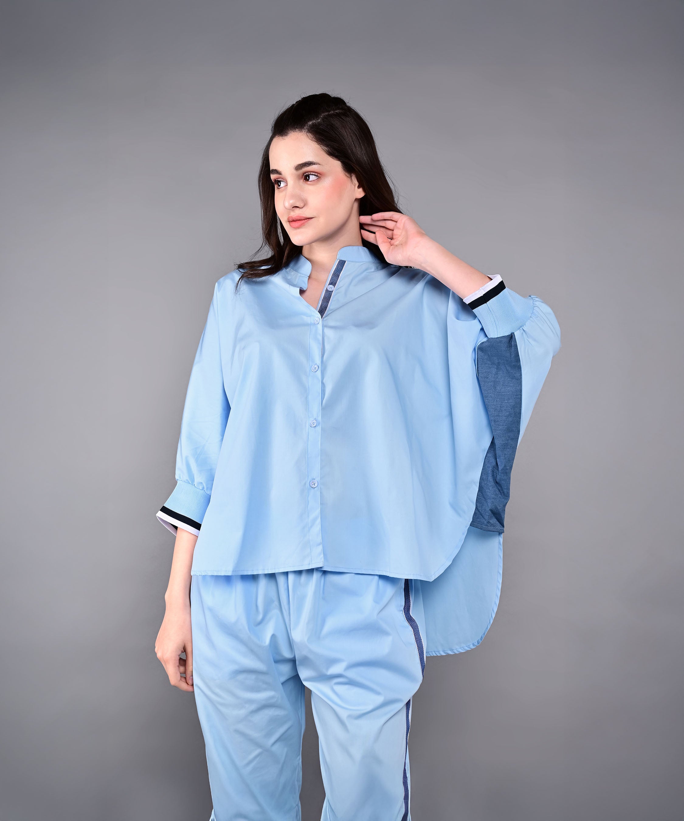 Woman wearing the Denim Accented Set, a loose light blue batwing sleeve shirt with matching joggers, made from 100% cotton, poses against a gray background.
