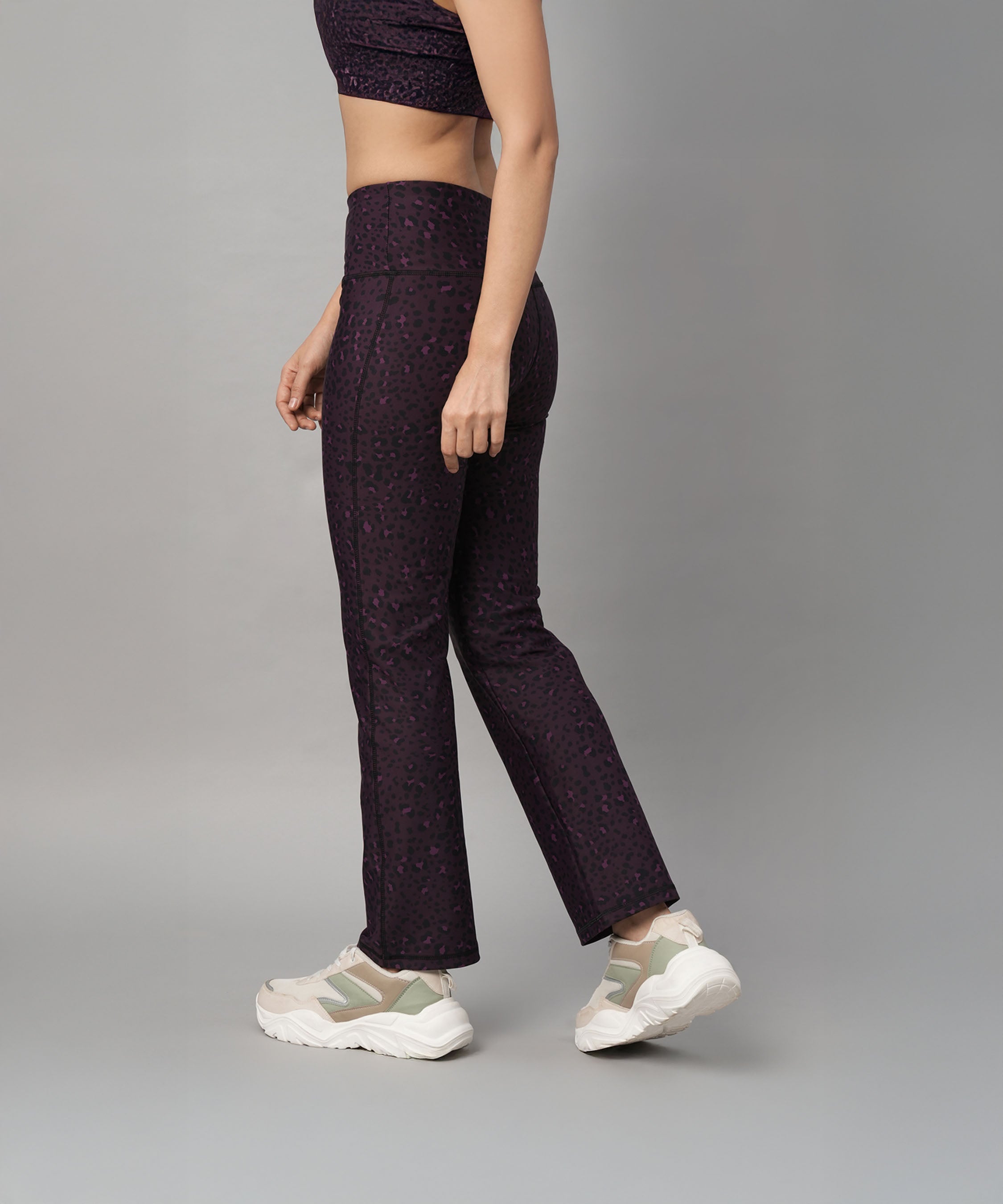 Woman in a matching activewear set featuring Pink Animal Print Wide Legged Leggings and white sneakers stands against a plain gray background.