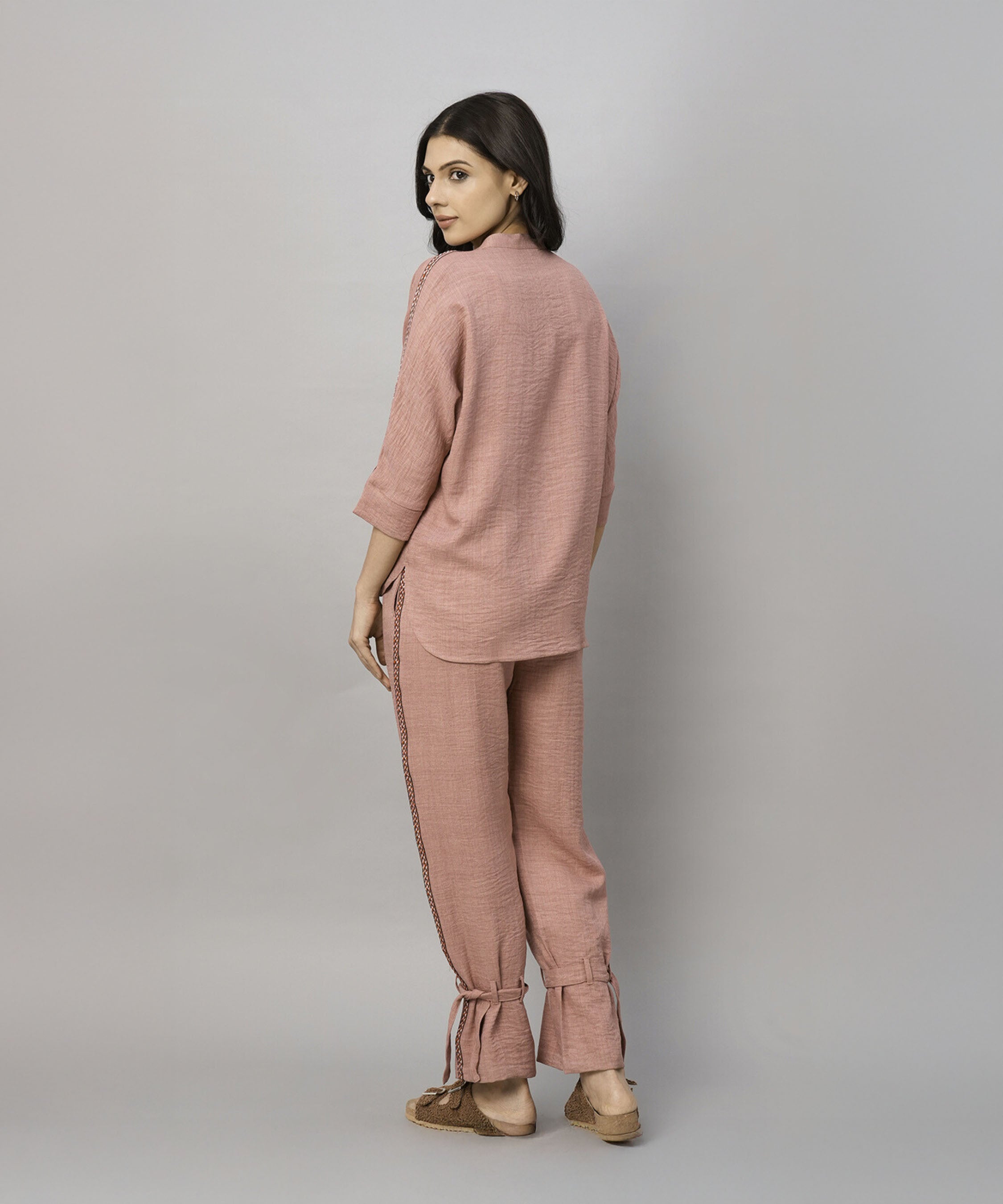 A woman wears the Vintage Pink Loose Shirt and Tie Up Pant Cord Set, made of 100% cotton, standing sideways and looking back against a plain gray background.