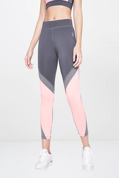 A woman stands indoors wearing Grey Leggings, a matching pink sports bra, and white sneakers.