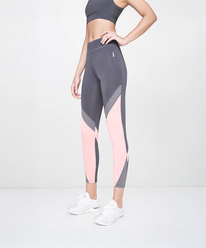 A woman wearing Grey Leggings, a gray sports bra, and white sneakers stands against a plain background.