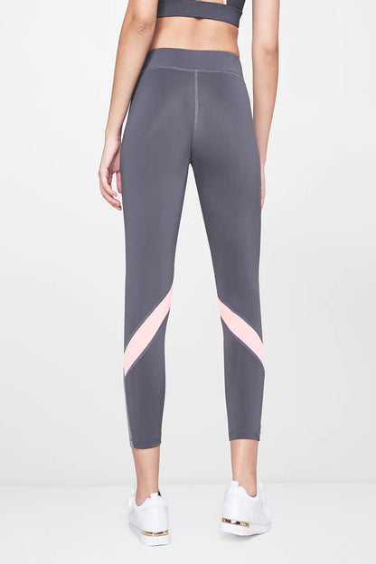 Woman wearing Grey Leggings, featuring pink stripes, paired with a matching sports bra and white sneakers, shown from the back.