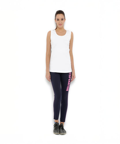 Woman standing, wearing a white sleeveless top, Tuna London Solid Women's Blue Track Pants, and black sneakers.