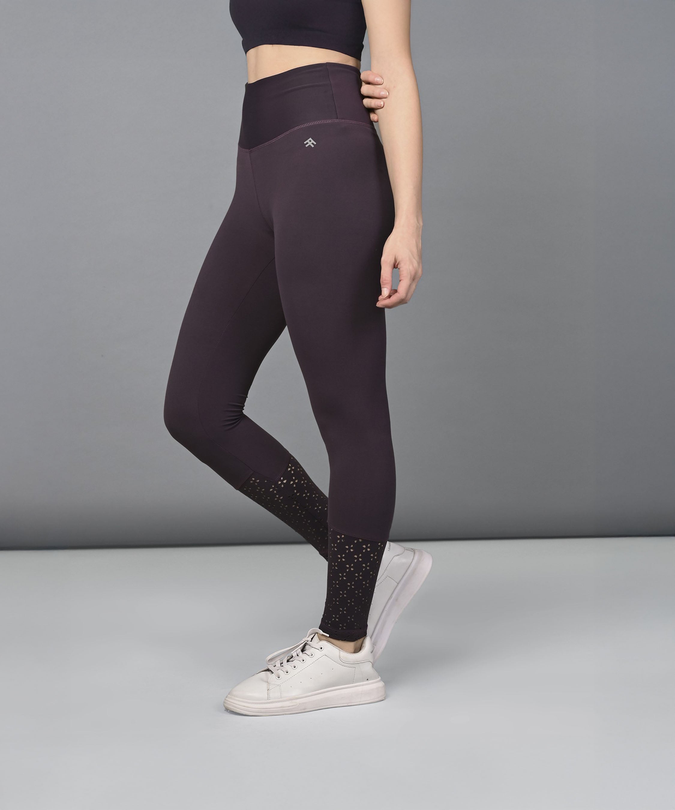 Woman wearing Wine Leggings and white sneakers stands against a plain gray background.