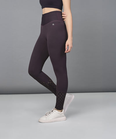 Woman wearing Wine Leggings and white sneakers stands against a plain gray background.