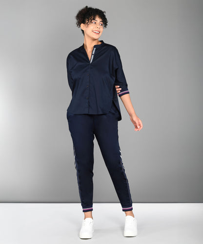 Woman wearing the Accented Set—a navy cotton co-ord featuring a button-up shirt and matching pants—smiling against a plain gray background.