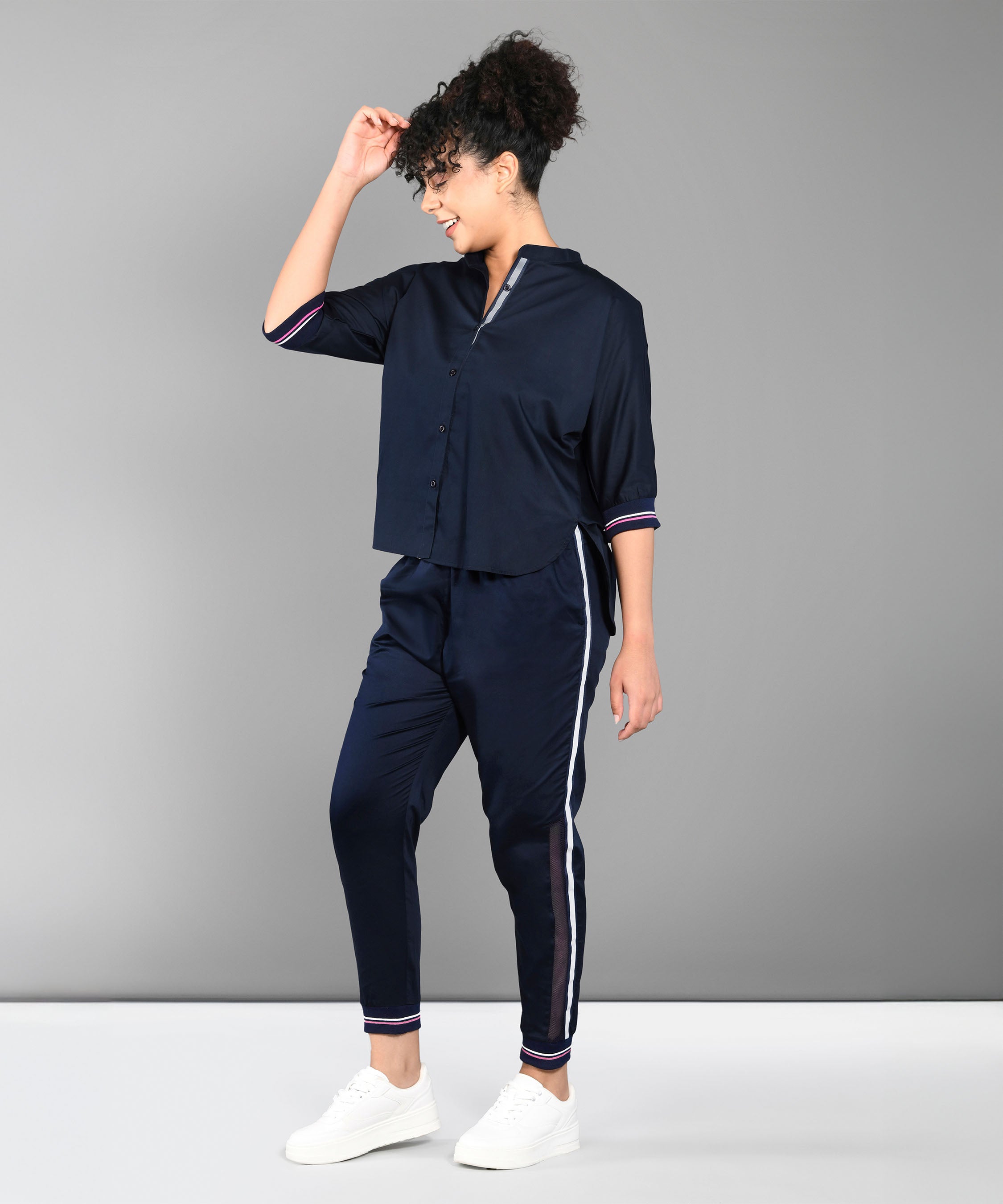 Woman in the Accented Set—a navy blue cotton co-ord with white stripes—paired with white sneakers, stands against a gray background.