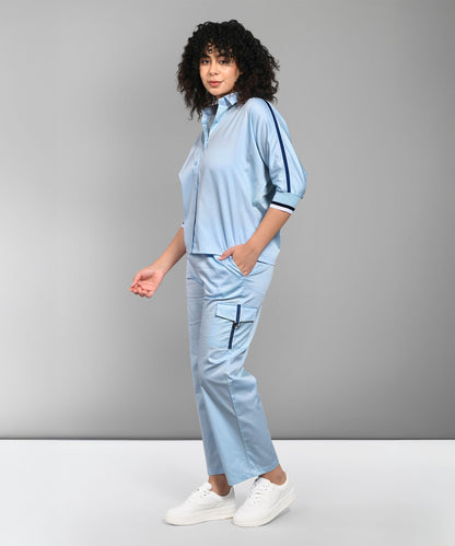 Woman modeling the Denim Chic Set, a light blue cotton co-ord featuring cargo track pants and a batwing sleeve shirt, styled with white sneakers against a plain gray background.