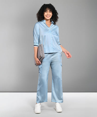 Smiling woman in the Denim Chic Set—a light blue batwing sleeve shirt and pants—holds a gray clutch against a gray background.