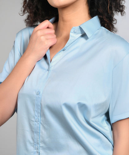 A person with curly hair wears the Denim Chic Set, a light blue batwing sleeve shirt, holding the collar near their neck.