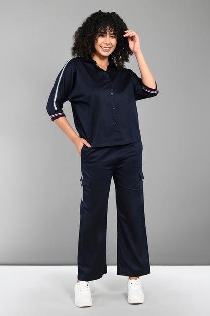 A smiling woman poses against a gray background wearing the Navy Blue Chic Set, featuring a navy batwing sleeve shirt and cargo track pants, paired with white sneakers.