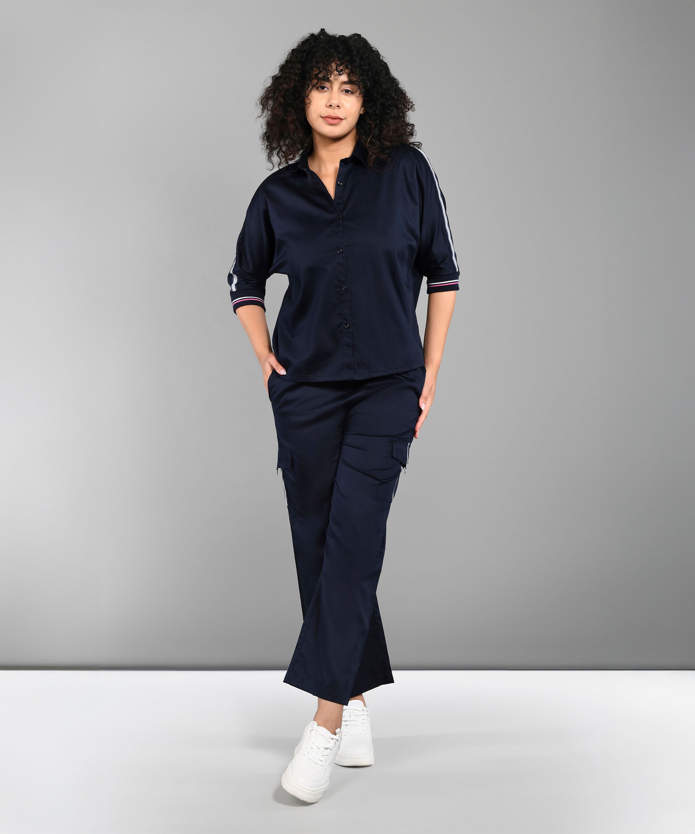 A woman with curly hair wears the Navy Blue Chic Set, featuring a navy shirt and track pants, standing against a gray background.