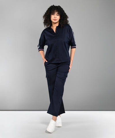 A woman with curly hair wears the Navy Blue Chic Set, featuring a navy shirt and track pants, standing against a gray background.