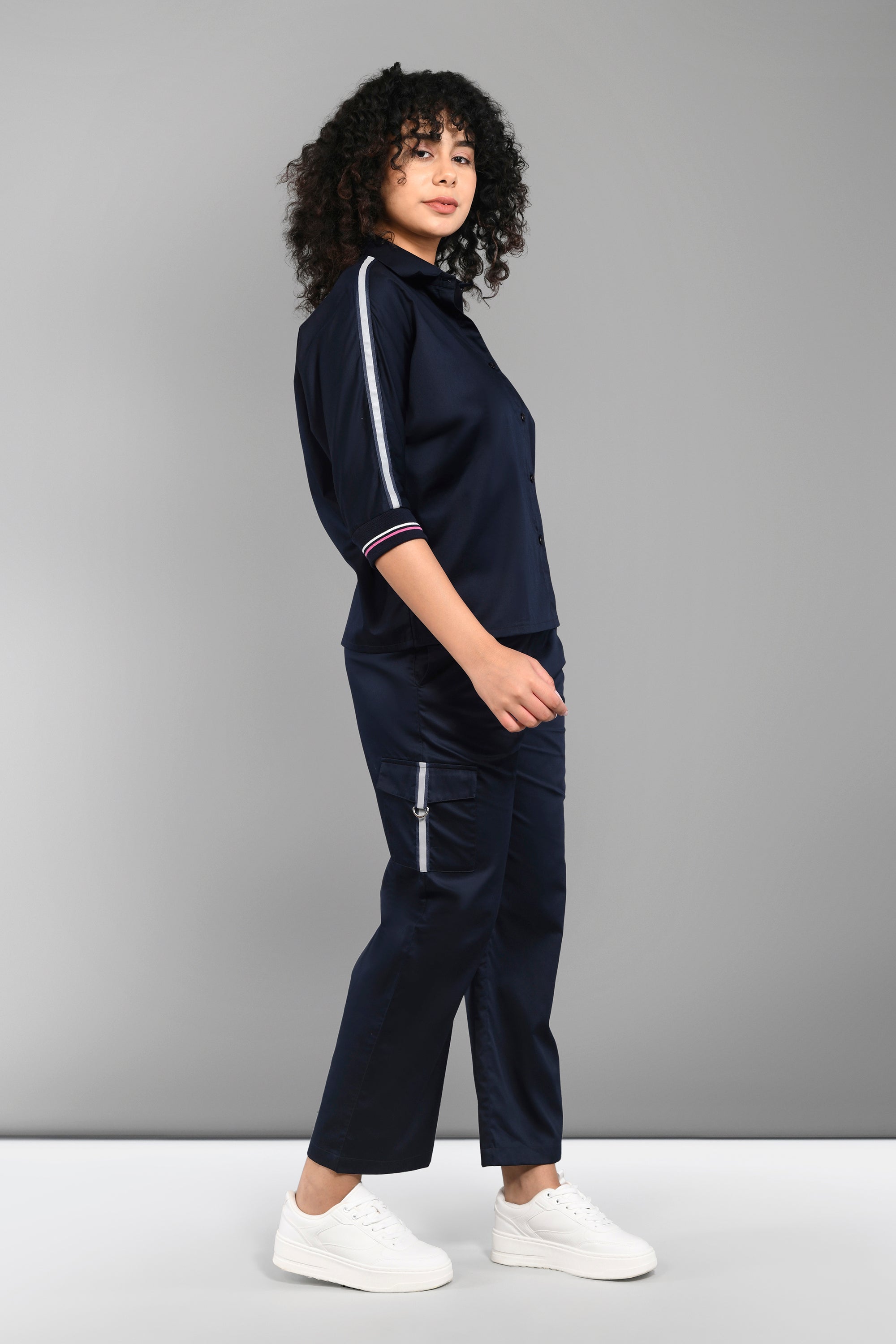 Woman wearing the Navy Blue Chic Set—a cotton co-ord with white stripes, featuring a batwing sleeve shirt and matching cargo track pants—stands sideways in white sneakers.
