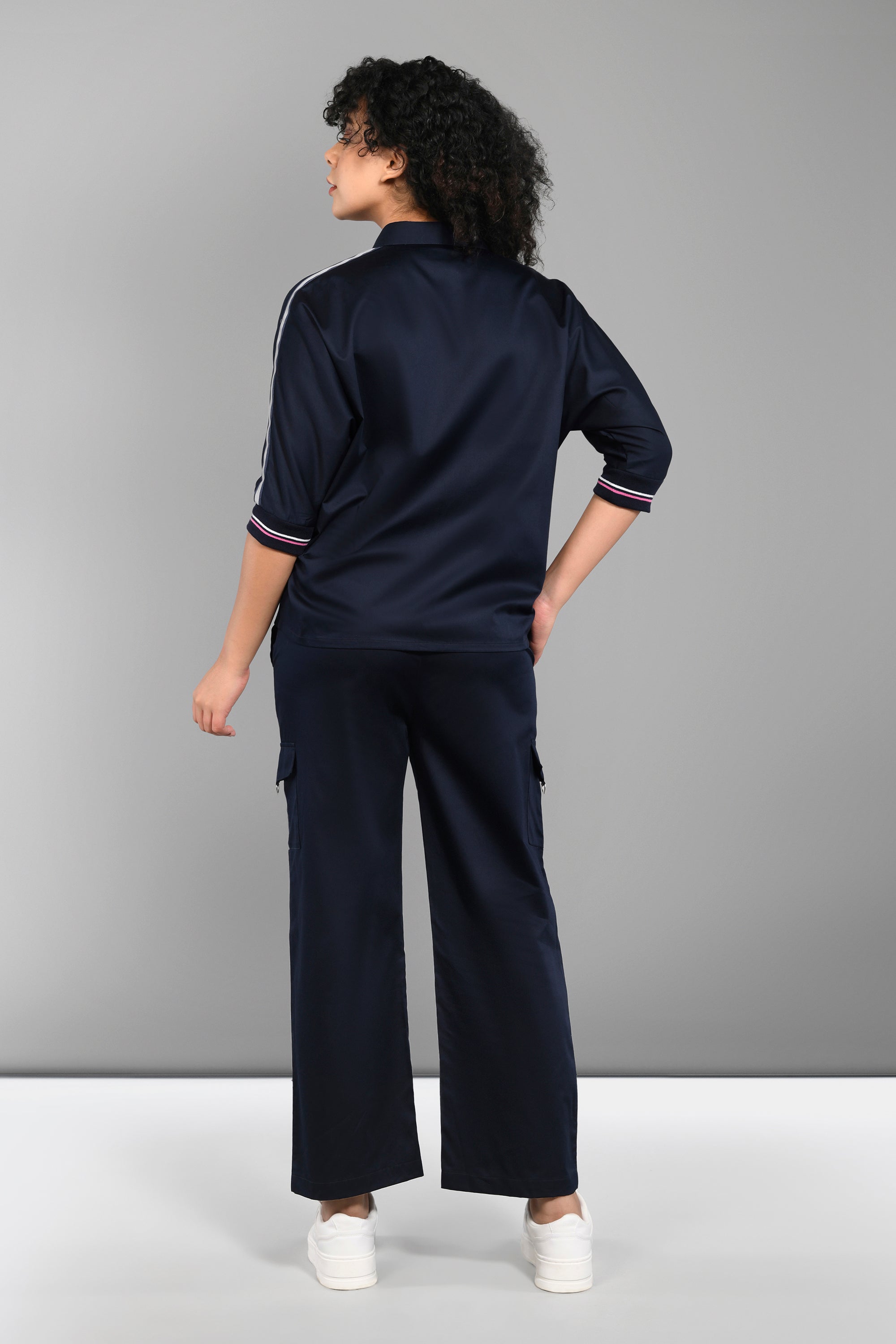 A person wearing the Navy Blue Chic Set with cargo track pants and white sneakers stands facing away against a gray background.