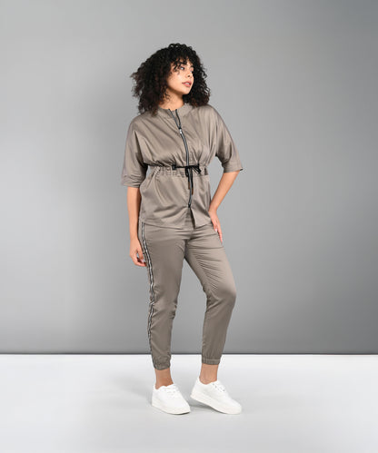 A woman in the Zipped Neutral Jacket Jogger set with a black zipper and white sneakers stands against a gray background.
