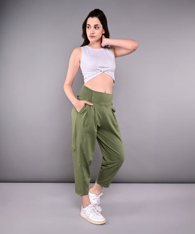 A woman poses with one hand on her hip in a White Twisted Crop Top and green pants against a gray background.