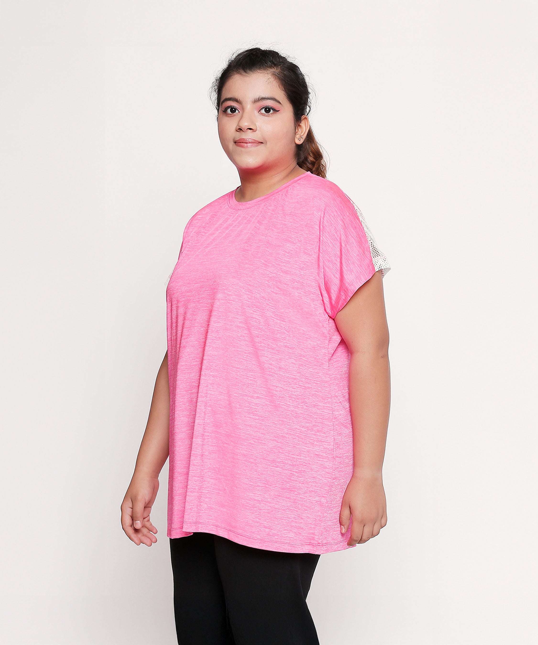 Woman wearing a loose Nova Sports Tee in pink and black pants, standing against a plain white background.