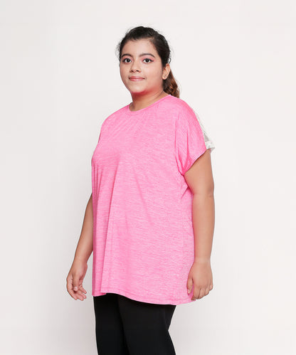 Woman wearing a loose Nova Sports Tee in pink and black pants, standing against a plain white background.