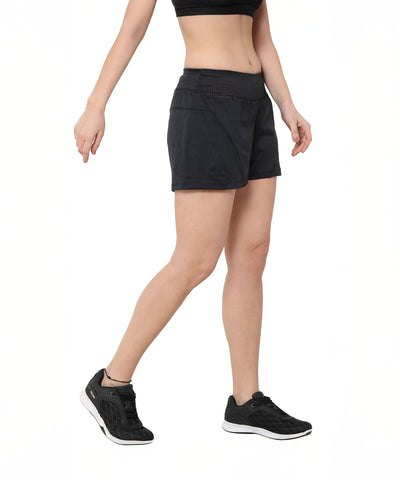 A woman poses against a white background wearing Black Shorts, a crop top, and sneakers; her outfit is crafted from breathable fabric for ultimate comfort.