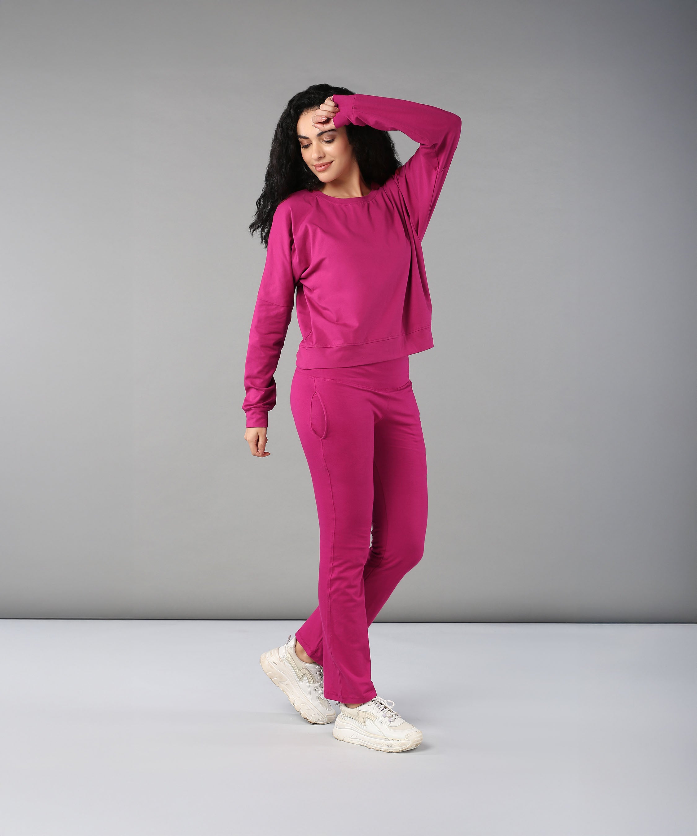 A woman models the Deep Pink Comfort Duo cotton lycra tracksuit, striking a confident pose with one hand on her forehead against a plain gray background.