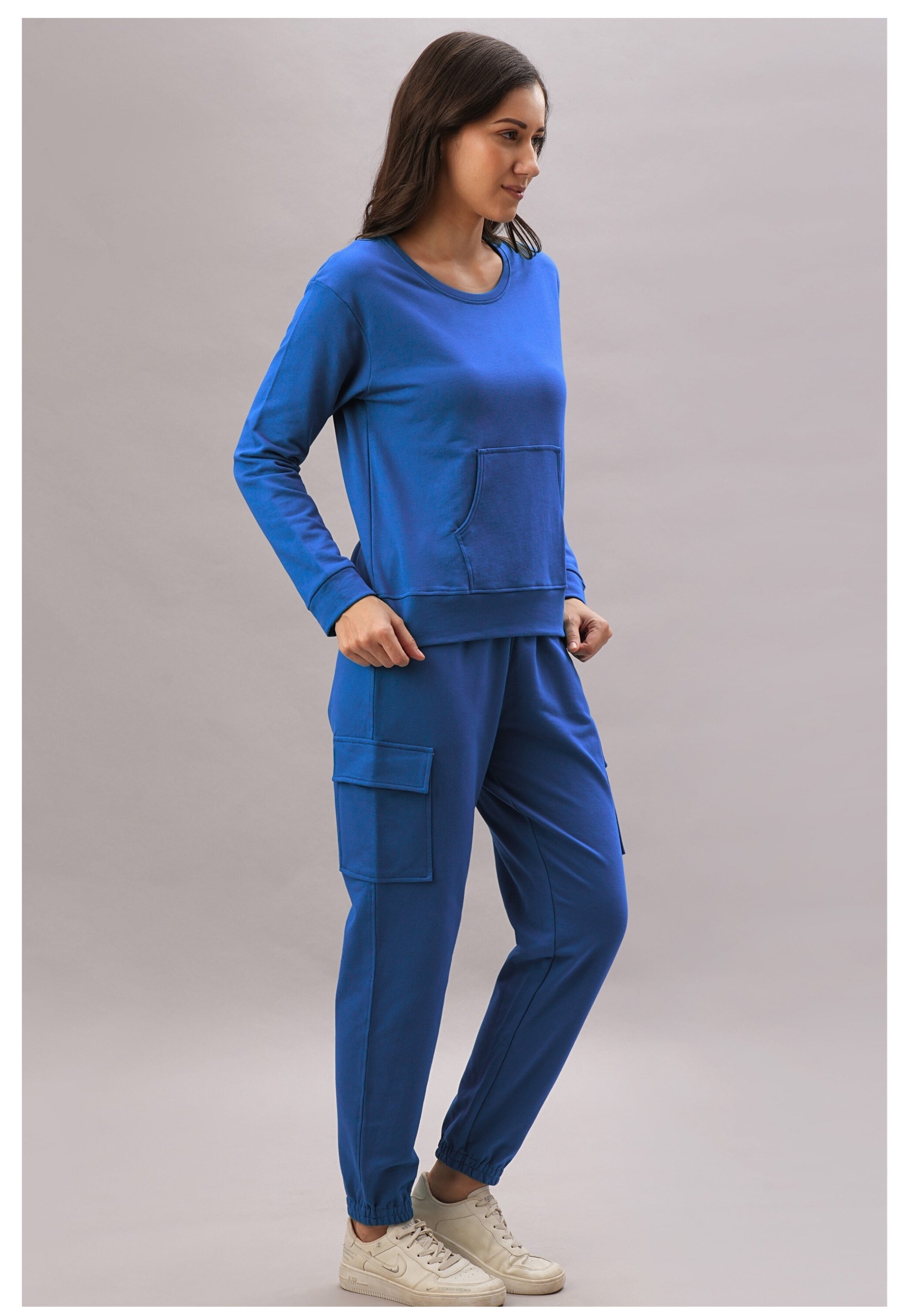A woman wears the Soft Royal Blue Trackset, featuring breathable cotton-viscose cargo joggers, paired with white sneakers and set against a plain background.