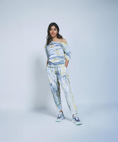Woman wearing the One Side Off-Shoulder + Yoga Pants set in yellow & grey with sneakers, standing against a plain light background, hands in pockets.