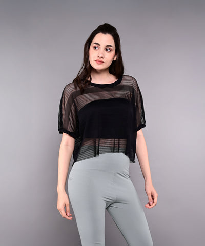 A woman wears the Tuna Active Black Netted Top layered over a black tank with light gray leggings, standing against a plain gray background.