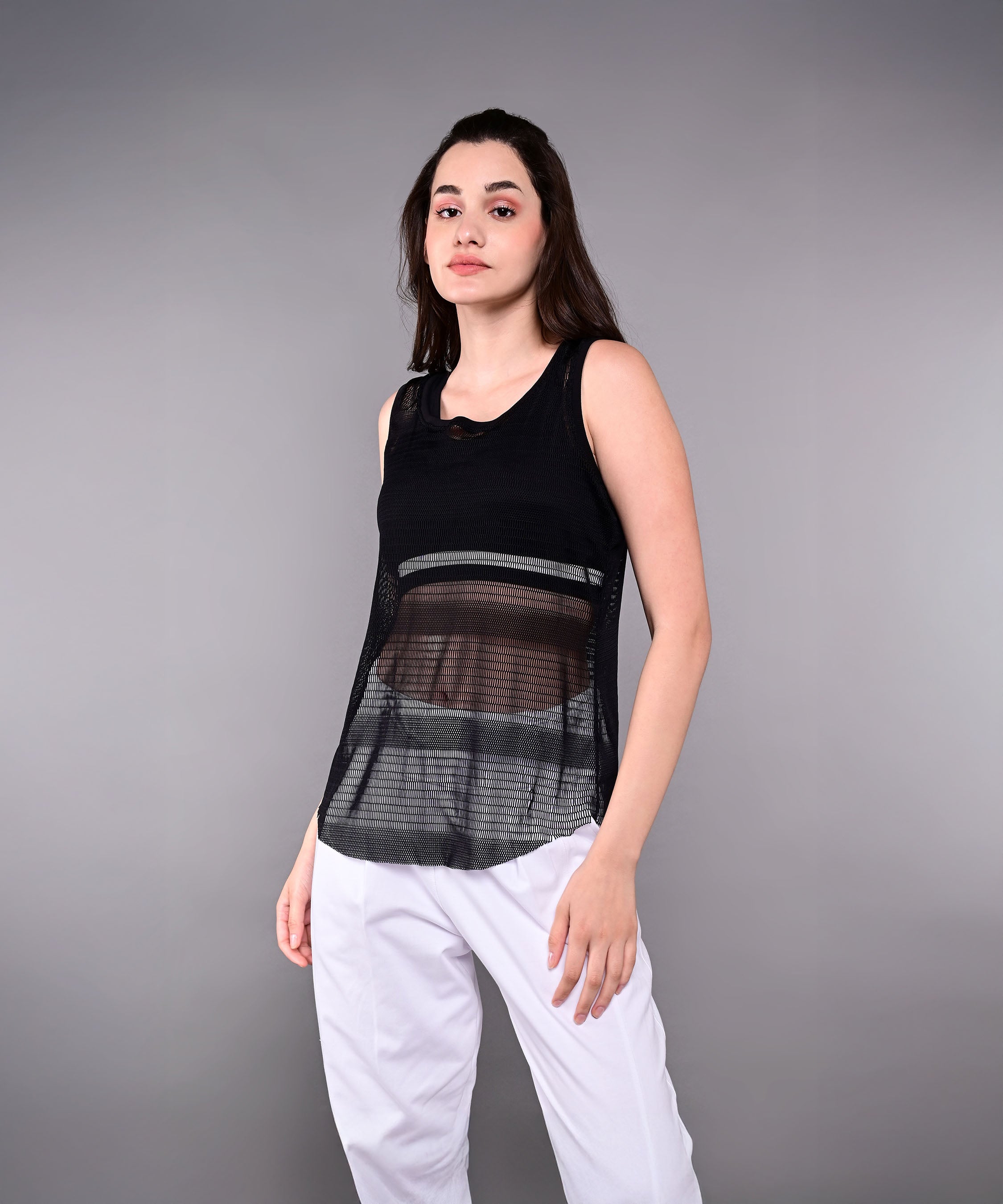 Woman wears the Tuna Active Black Netted Tank Top with white pants, standing against a plain gray background.