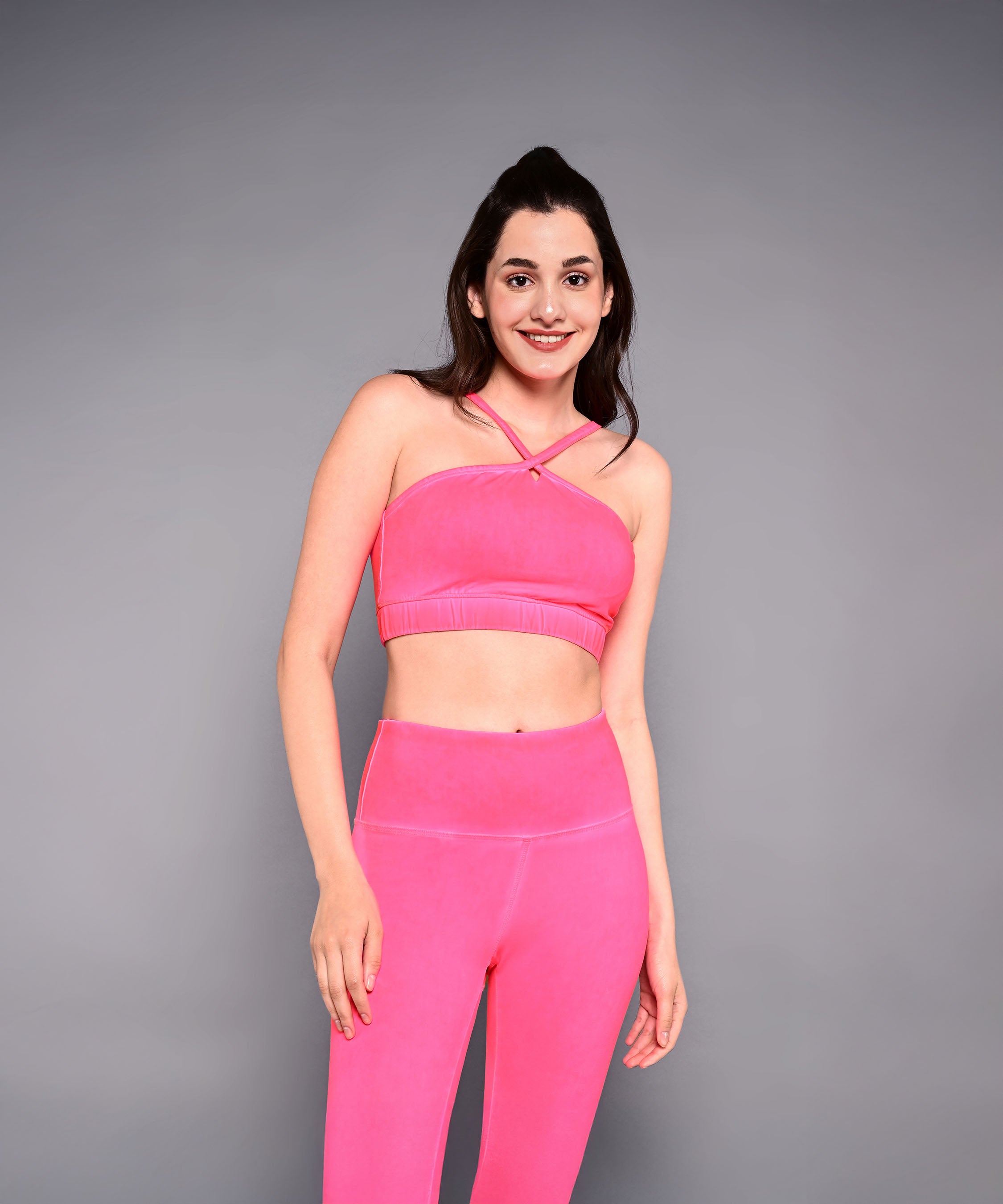 Woman wearing a Neon Pink Sports Bra, standing and smiling against a plain gray background.