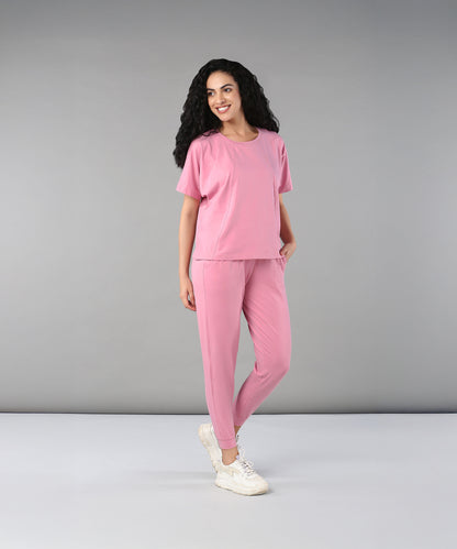 A woman with curly hair smiles against a plain background, wearing the Flamingo Pink Chic Ensemble. The buttery soft fabric brings comfort and style to her look.