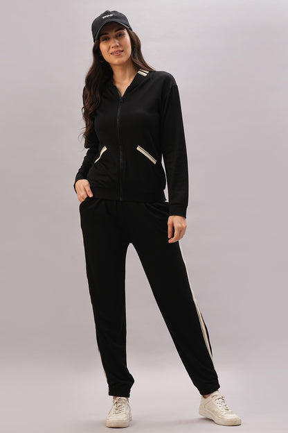 Woman wearing a Black Co-Ord Set with a stylish top, paired with white sneakers and a black cap, standing against a light gray background.