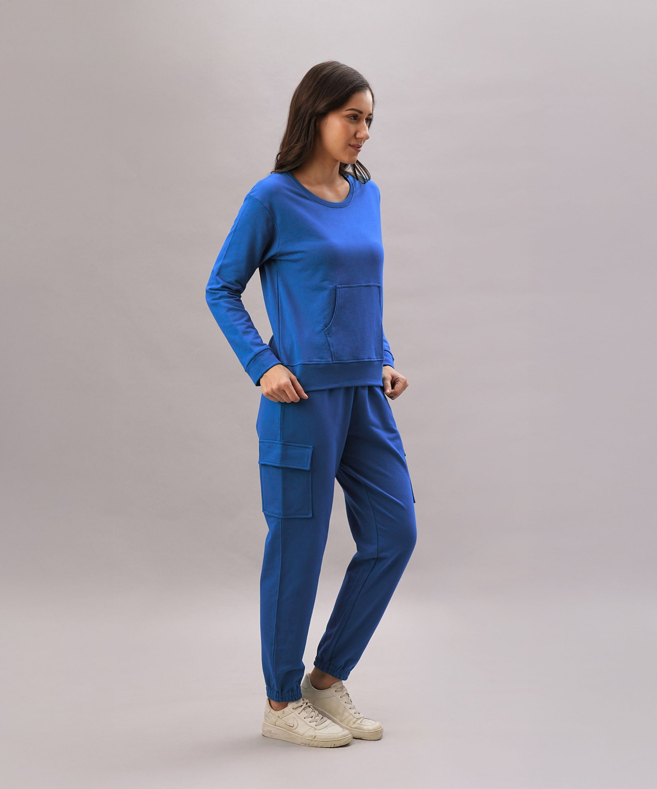 A woman wears the Soft Royal Blue Trackset, featuring breathable cotton-viscose cargo joggers, paired with white sneakers and set against a plain background.