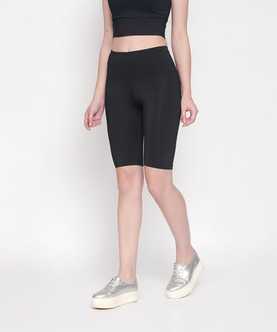 A woman wears Black Biker/Cycling Shorts with a high-rise waistband, styled with a black crop top and silver platform sneakers, set against a white background.