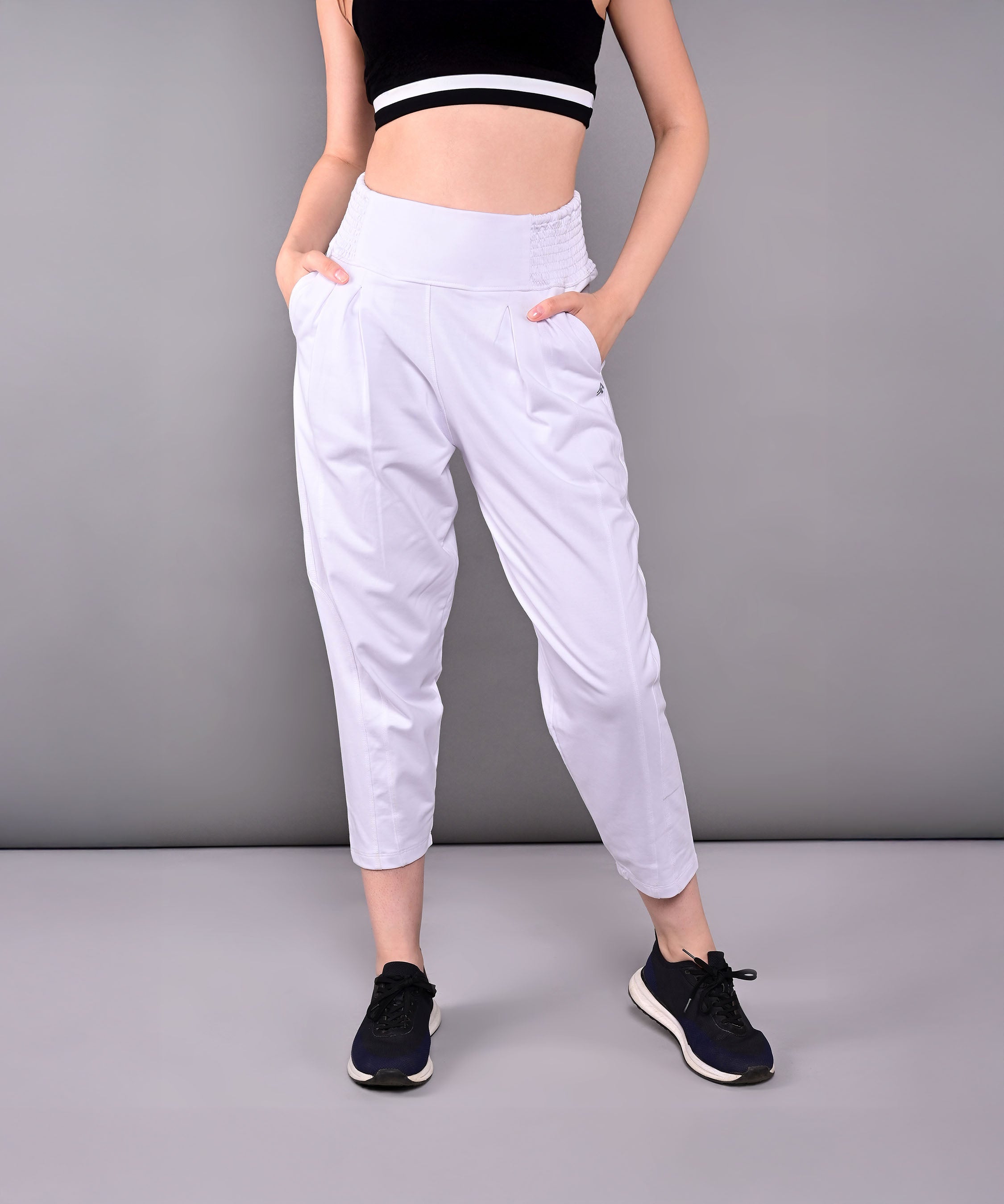 Woman in black crop top and Pleated Yoga Pant With Smocked Waistband, featuring white pleats and pockets, standing against a gray background.