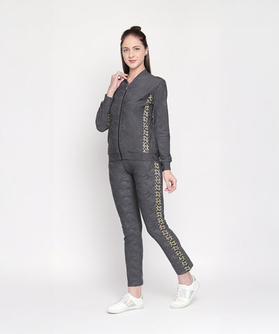 A woman in athleisure poses against a plain white background, wearing Self Printed Grey TrackPants with gold detailing.