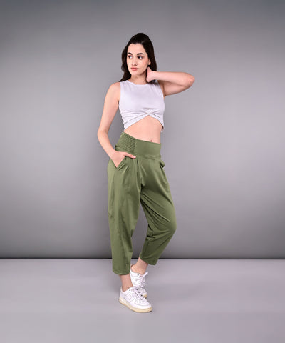 Woman wears green Pleated Yoga Pant With Smocked Waistband, featuring pleats and a high waist, paired with a gray sleeveless crop top and white sneakers.