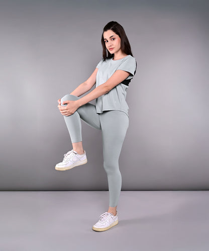A woman showcases the Dynamic Grey Performance Set, standing on one leg and holding her raised knee against a plain gray background.