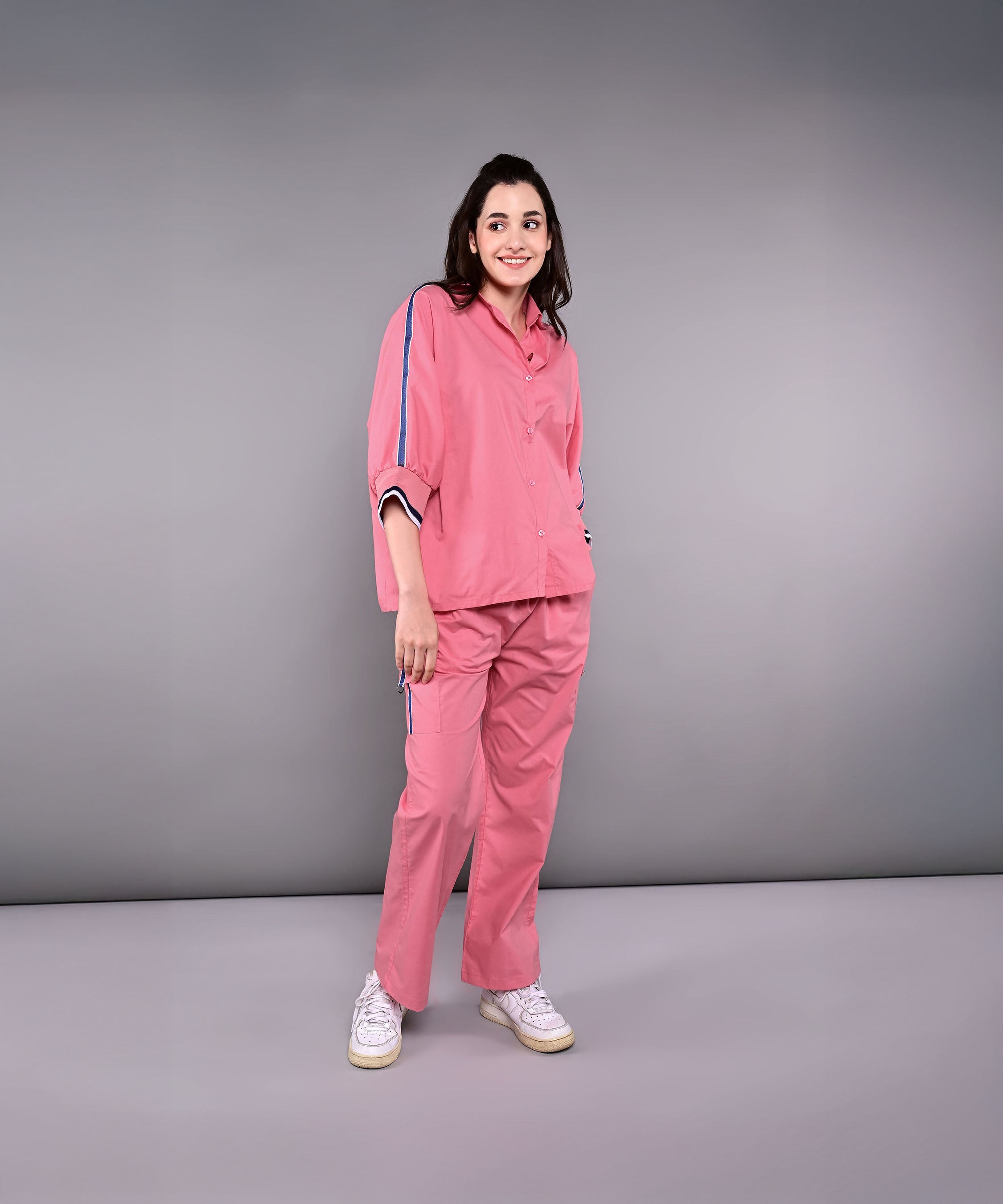 A woman smiles in front of a plain gray background, wearing the Effortlessly Chic Set—a pink cotton co-ord featuring blue stripes.