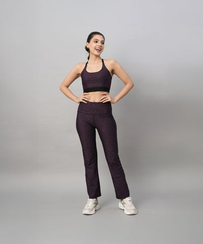 A woman in matching dark workout clothes stands smiling with hands on hips, highlighting the Pink Animal Print Sports Bra against a plain background.