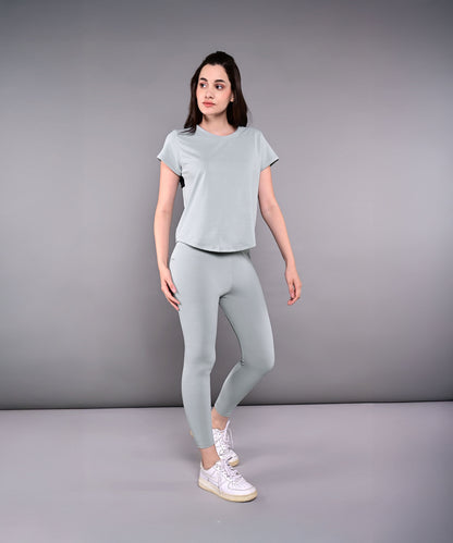 A woman stands in a studio wearing the Dynamic Grey Performance Set—athletic leggings and a grey racerback top with moisture-wicking properties—against a neutral background.