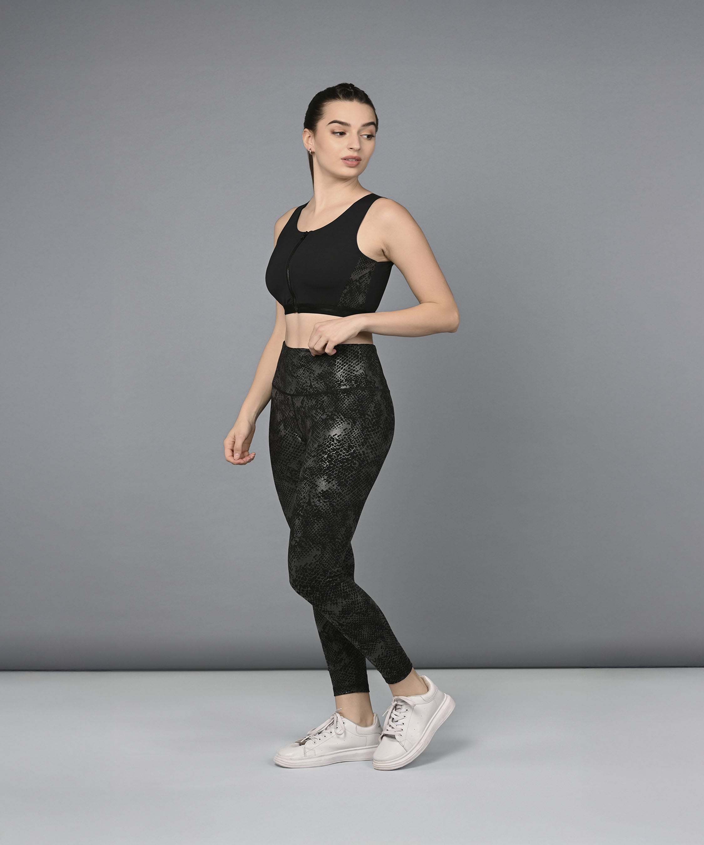 A woman models the Zipped Sports Bra & Metallic Legging set, posing confidently against a plain grey background.