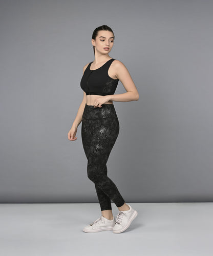 A woman models the Zipped Sports Bra & Metallic Legging set, posing confidently against a plain grey background.