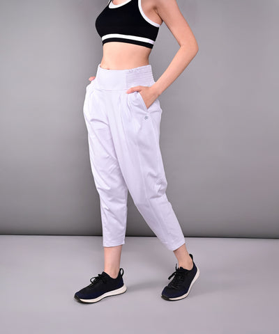 Woman wearing a black sports bra, black sneakers, and Pleated Yoga Pant With Smocked Waistband in white against a grey background.