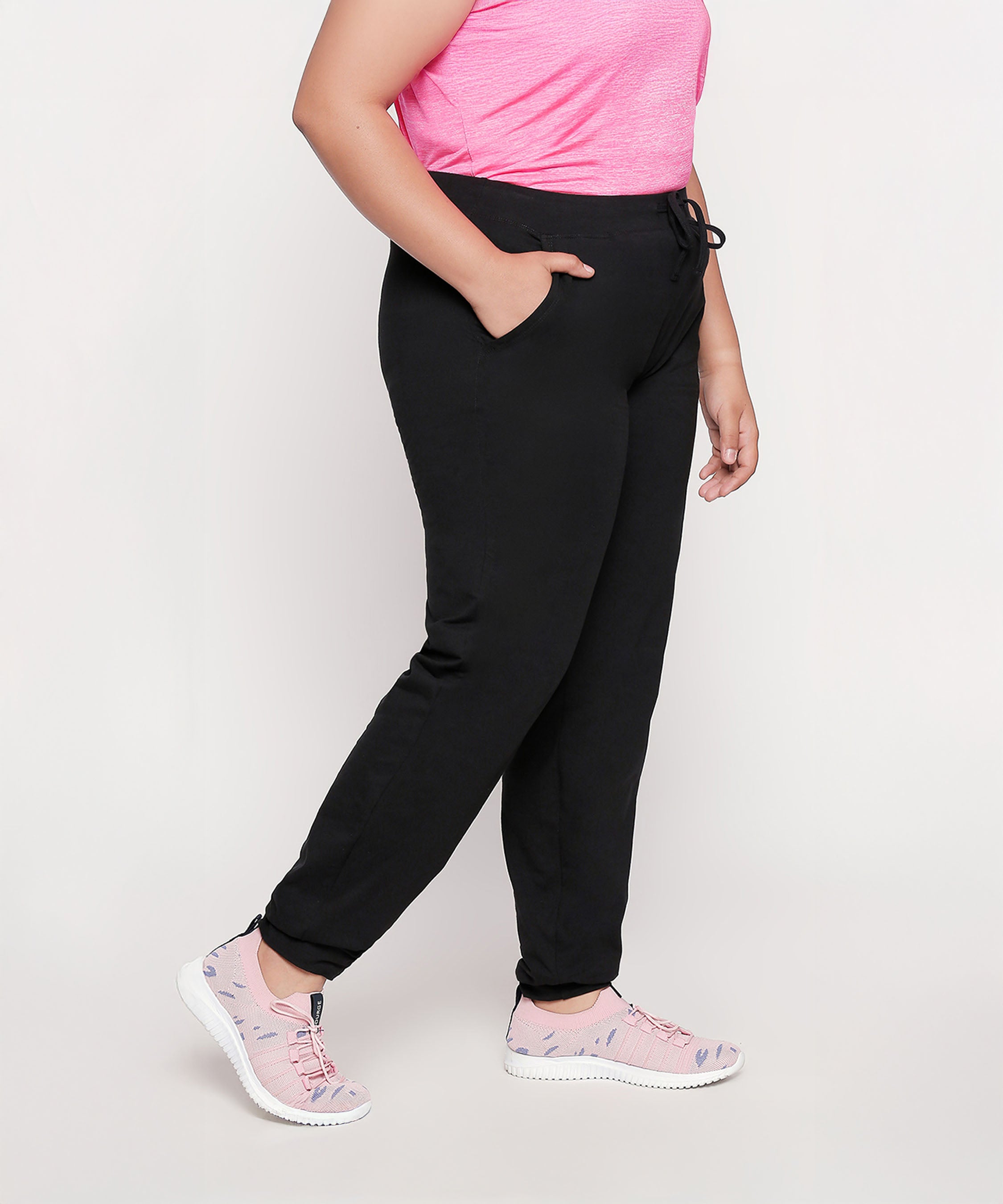 Person wearing a pink shirt, Classic Joggers - Plus Size 02, and pink sneakers, standing with hands in pockets.
