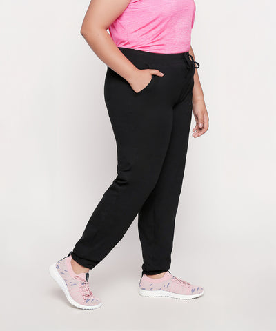 Person wearing a pink shirt, Classic Joggers - Plus Size 02, and pink sneakers, standing with hands in pockets.